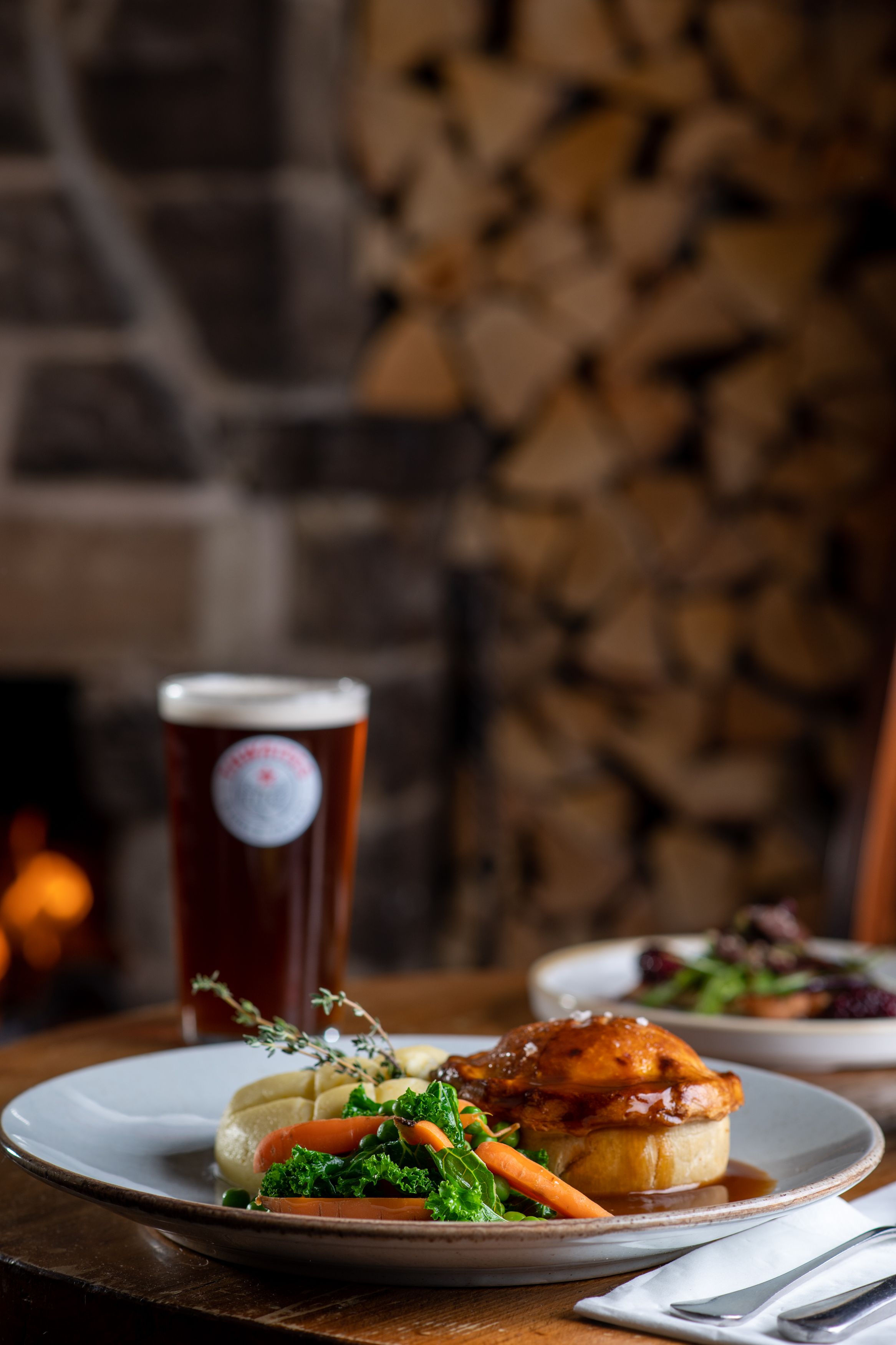 Pie, mash, vegetables and gravy with a pint of thwaites ale in the background in front of fire