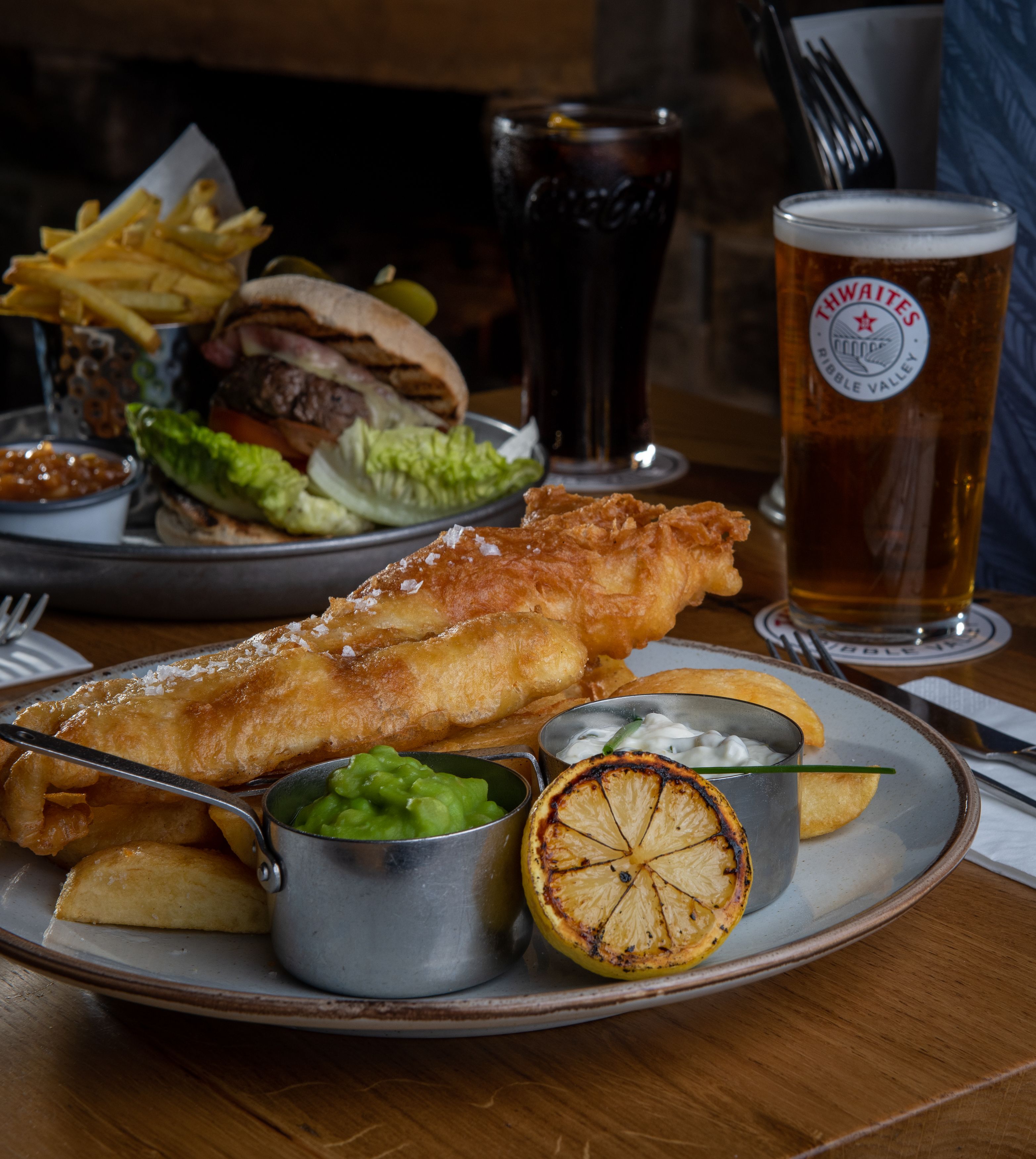 fish and chips and burger on table with a pint of thwaites ale and coke