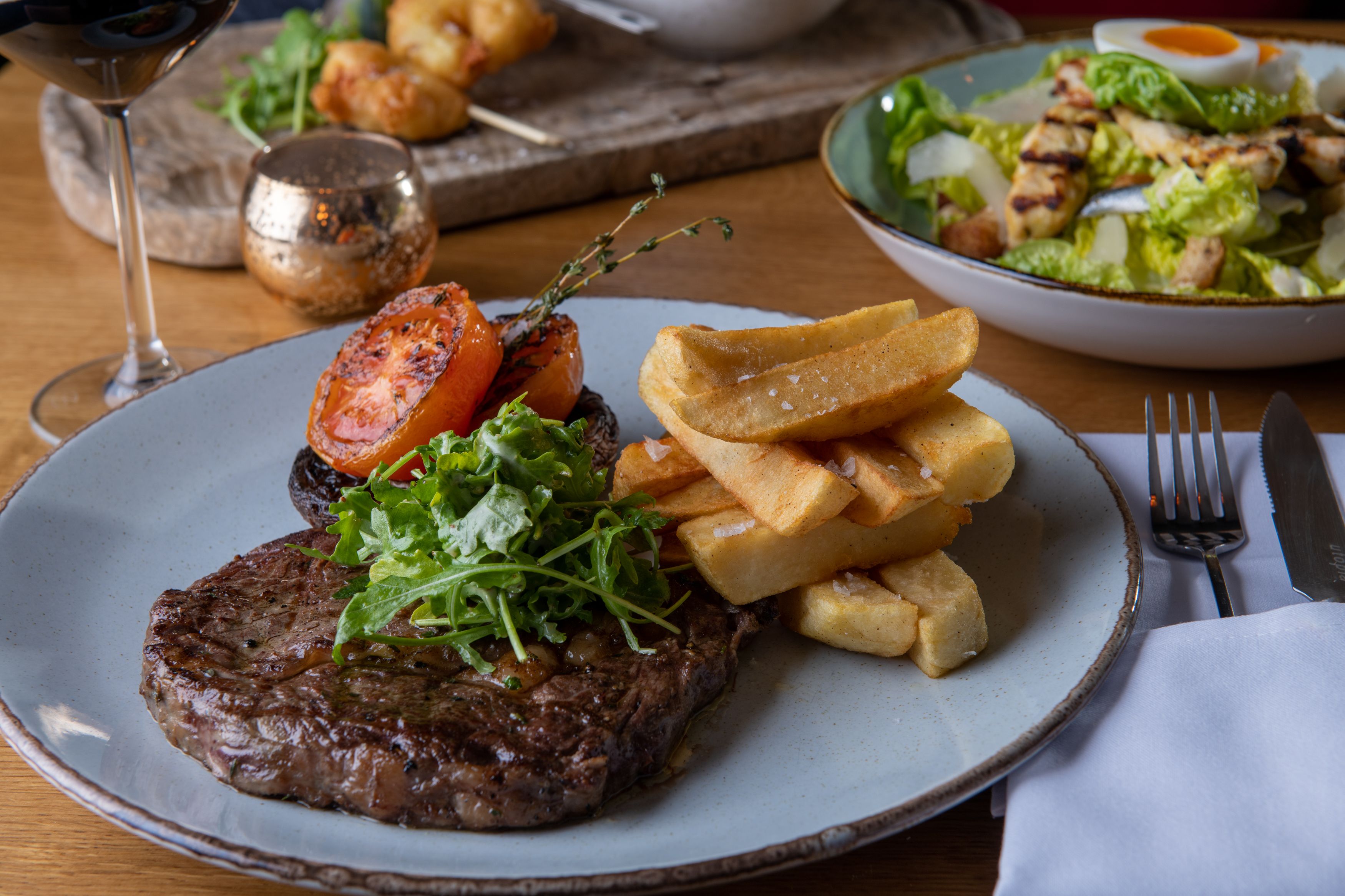 Steak and chips on table with wine and salad in background
