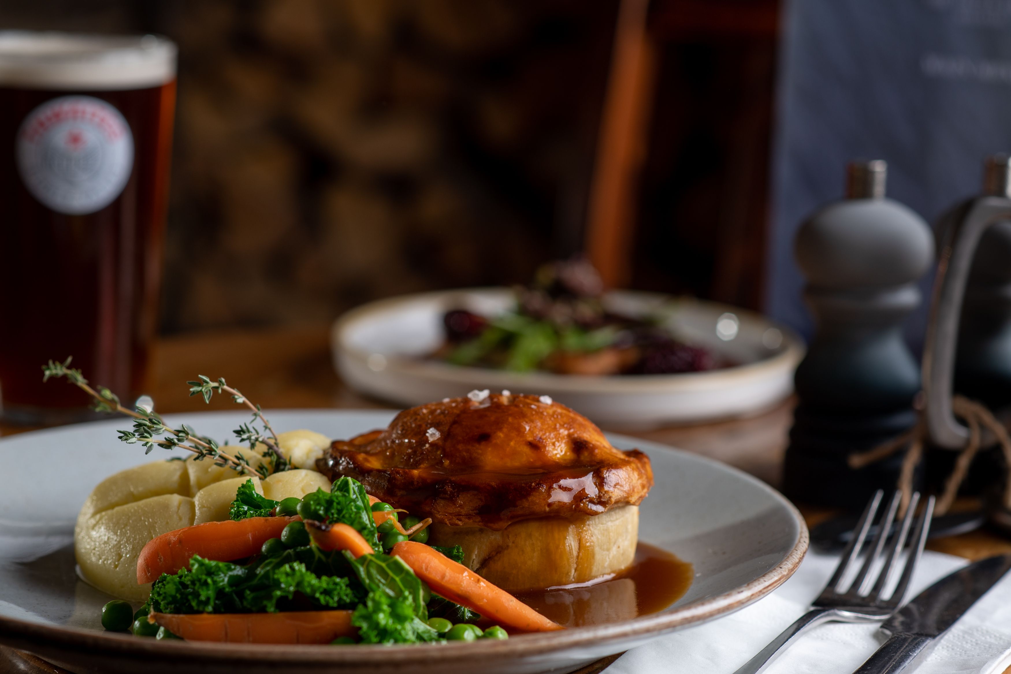 Pie, mash, vegetables and gravy with a pint of thwaites ale in the background