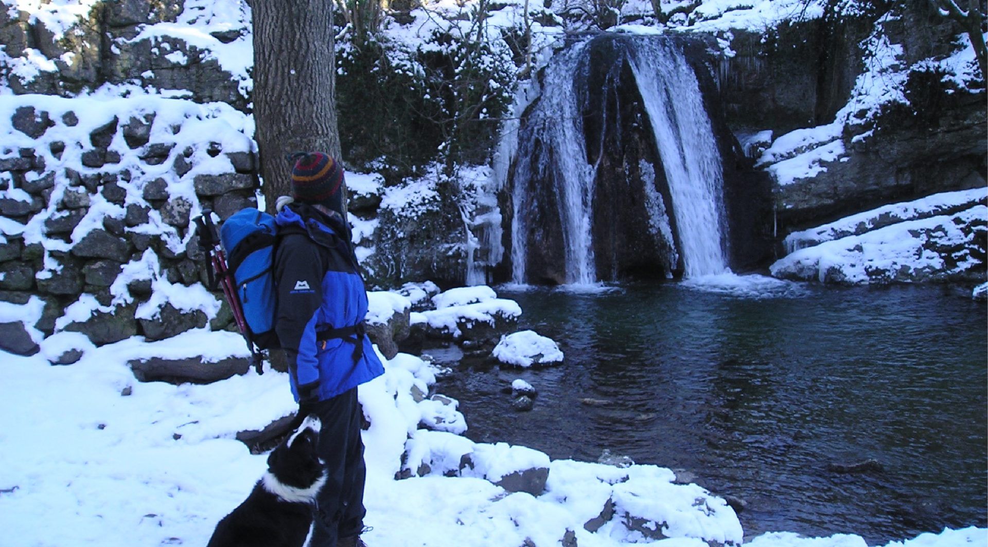 person walking dog next to snowy waterfall